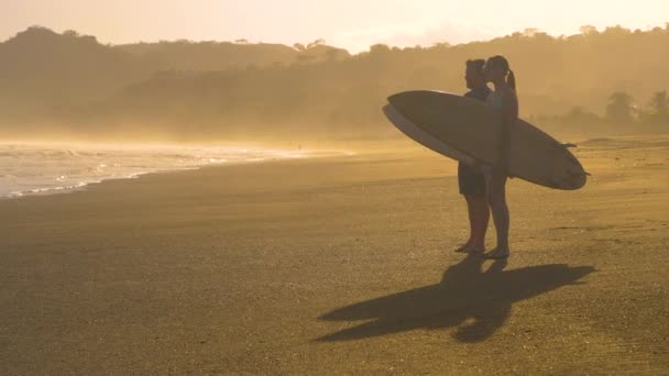 SLOW MOTION: Δύο surfers στέκονται στην παραλία και ελέγχουν τα κύματα πριν το surfing. Surf spot analysis πριν paddling έξω για τα κύματα. Παραλία lifestyle shot σε όμορφο χρυσό φως. - Πλάνα, βίντεο