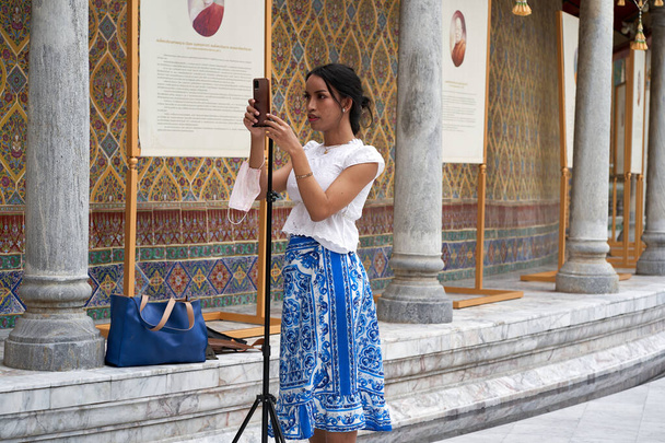 Transsexual tying a mobile phone to a tripod in front of a Buddhist temple in Thailand - Foto, imagen