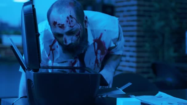 Dumb brain-eating monster with blood on clothes photocopying his own face at night. Spooky doomsday evil looking zombie with bloody wounds damaging photocopy electronic machine in company workspace - Πλάνα, βίντεο