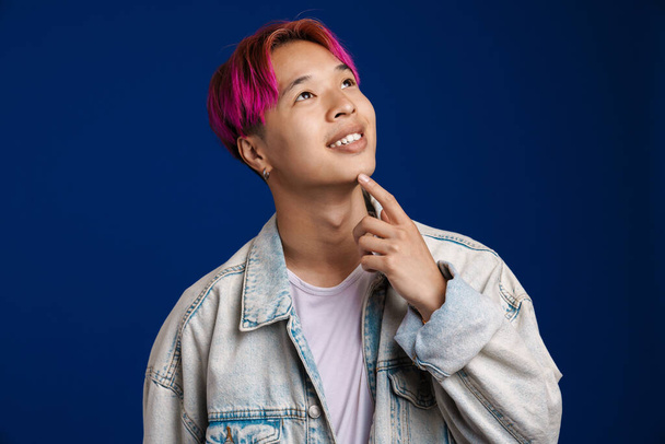 Asian boy with pink hair smiling and looking upward isolated over blue background - Fotó, kép