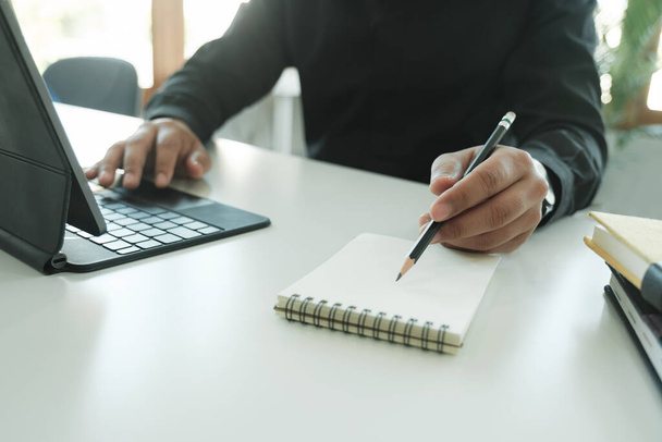 Gros plan homme d'affaires travaillant sur tablette numérique et ordinateur portable en utilisant stylo stylet sur table blanche. - Photo, image