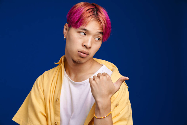 Asian boy with pink hair looking and pointing finger at camera isolated over blue background - Photo, Image