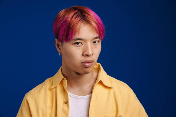 Asian boy with pink hair posing and looking at camera isolated over blue background - Foto, imagen