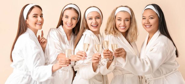 Belle giovani donne in accappatoi bere champagne su sfondo di colore chiaro - Foto, immagini