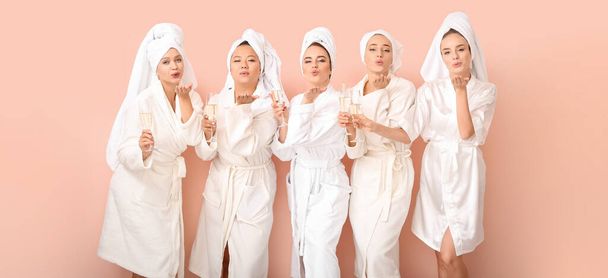 Beautiful young women in bathrobes drinking champagne and blowing kiss on color background - Foto, Bild