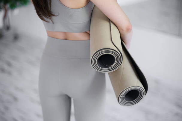 Молода красива жінка тримає килимки для йоги, стоячи в легкій студії. Вид ззаду. Концепція молоді, краси та здорового способу життя
. - Фото, зображення