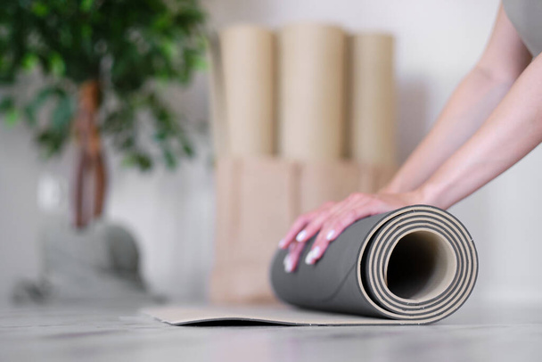 Großaufnahme einer Frauenhand, die eine Gymnastikmatte hochrollt. Yoga-Studio. Das Konzept eines gesunden Lebensstils. - Foto, Bild