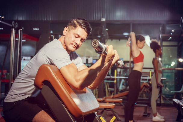 Fitness mężczyzna podnoszenie ciężarów w siłowni fitness, grupa z hantlami urządzenia treningowe na siłowni sportowej - Zdjęcie, obraz