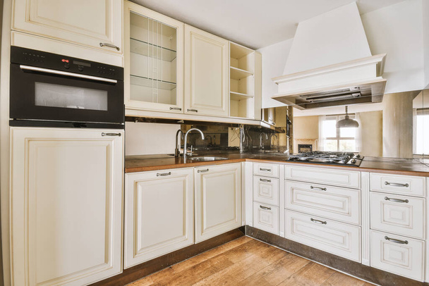 Keukenhoek met wit meubilair, gespiegeld schort, moderne apparatuur en afzuigkap - Foto, afbeelding
