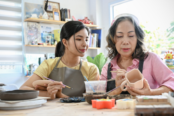 Professionale invecchiato donna asiatica formazione di una giovane femmina per disegnare e dipingere una tazza di ceramica in officina. Concetto laboratorio di pittura ceramica - Foto, immagini