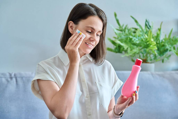 Young woman cleans her face with cotton pads, using cleansing cosmetic milk lotion tonic. Beauty, skin care, professional medical cosmetics concept - Foto, immagini