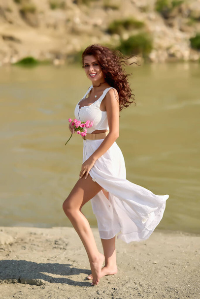 Beautiful woman in white dress on the bank of a river in summer. - 写真・画像