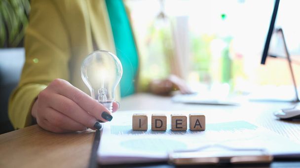 Close-up of woman holding lightbulb and word idea collected with wooden cubes. New business development solution concept - Photo, Image