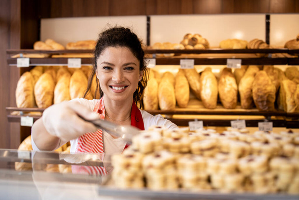 Portrét pracovnice pekárny prodávající vynikající sušenky. V poličkách na pozadí s chlebem. - Fotografie, Obrázek