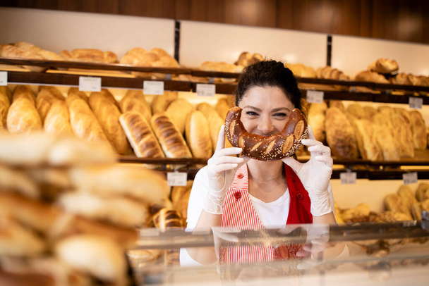 Portret van een bakker die een grappig lachend gezicht maakt met croissant in de bakkerij. - Foto, afbeelding