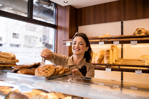 Mujer bonita en delantal vendiendo pastelería dulce recién horneada y pan en panadería. - Foto, imagen