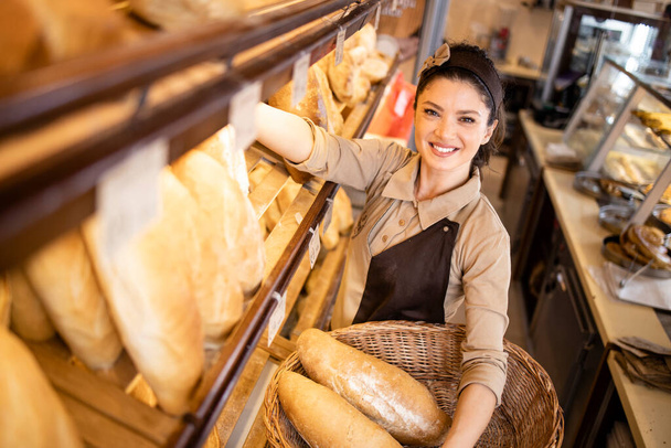 Top widok sprzedawcy piekarni organizujących świeże bochenki chleba na półkach w piekarni. - Zdjęcie, obraz
