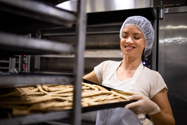Female baker standing by the metal tray and preparing raw pastry for baking. - Foto, Bild