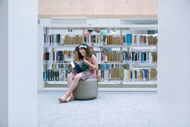Girl sitting on a Pouf reading at Gabriel Garcia Marquez Public Library in Barcelona. Empty copy space for Editor's text. - Fotó, kép