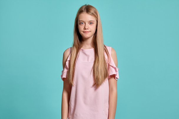 Studio portrait of a graceful blonde teenager in a pink t-shirt on blue background in various poses. She expresses different emotions posing right in front of the camera, smiling and looking satisfied - Фото, изображение