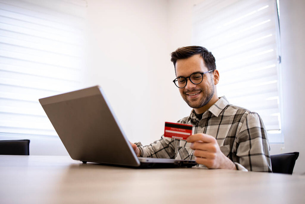 Przystojny mężczyzna kaukaski przy użyciu laptopa i karty kredytowej do e-bankowości lub zakupów online. - Zdjęcie, obraz