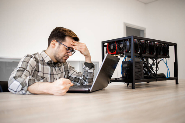 Programmer checking bitcoin value and earnings by his cryptocurrency mine and feeling disappointed. - Photo, Image