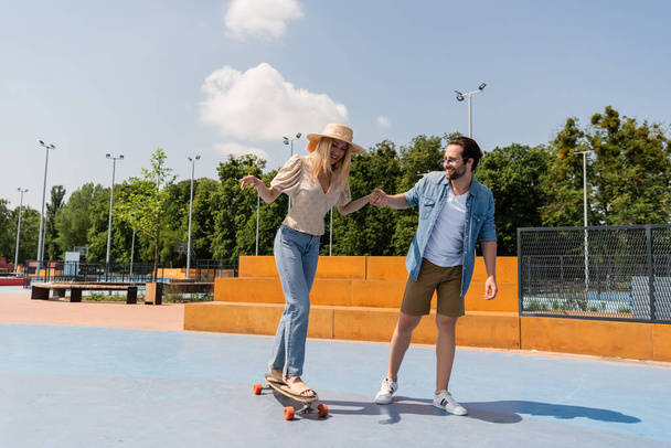 Cheerful couple riding longboard in skate park  - Фото, изображение