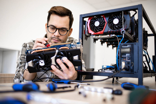 Caucasian man expert changing cooling fans on graphics card and maintaining bitcoin mining rig. - Photo, Image