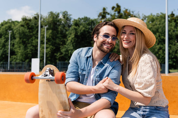 Positive couple holding hands and longboard in skate park  - Zdjęcie, obraz