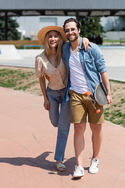 Positive couple hugging and holding longboard in park  - Zdjęcie, obraz