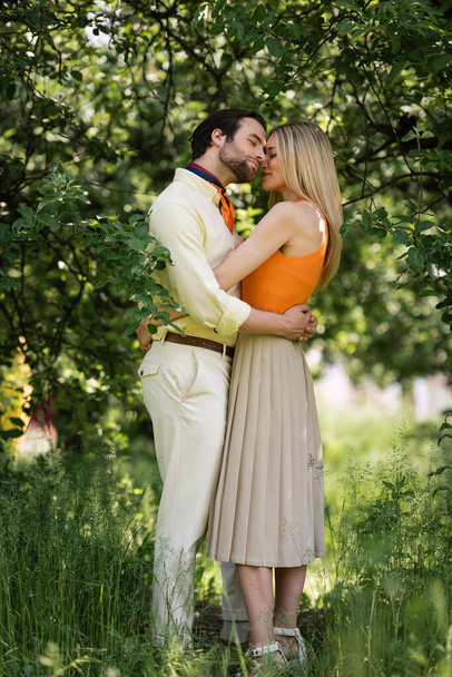 Side view of stylish couple embracing near trees in summer park  - Foto, Imagen