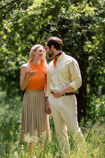 Mujer sonriente hablando con un novio elegante mientras camina en el parque de verano  - Foto, imagen