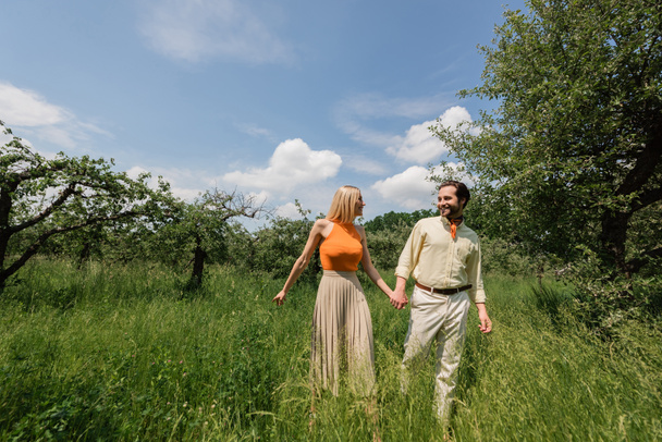 Romantisches Paar hält Händchen beim Spaziergang auf Wiese im Sommerpark  - Foto, Bild