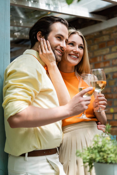 Stylish woman touching face of smiling boyfriend with wine in outdoor cafe  - Foto, Imagem