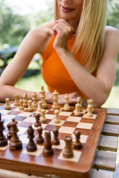 Vista recortada de la mujer sentada cerca del tablero de ajedrez en el parque  - Foto, Imagen