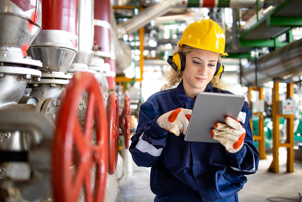 Trabajador de refinería con casco y orejeras comprobando los parámetros en la tableta para la producción de petróleo y gas. - Foto, imagen