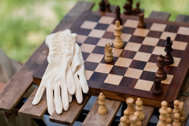 Рукавички біля дерев'яних фігур на шаховій дошці в парку
  - Фото, зображення