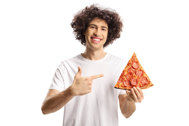 Happy young man holding a slice of pizza and pointing isolated on white background - Фото, зображення