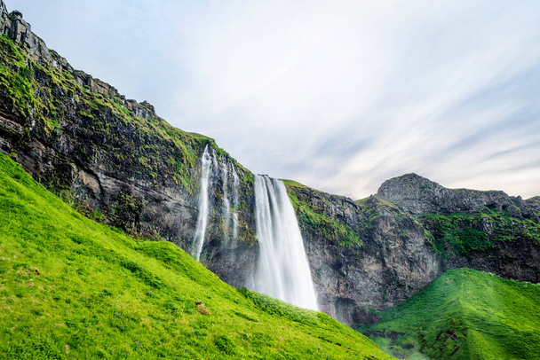 Seljalandsfoss waterfalls in Iceland with green hills and lava cliffs - Фото, изображение