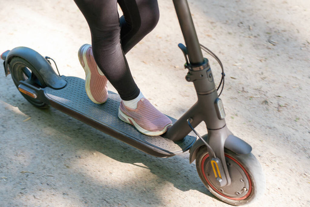 Petite fille monte un scooter électrique sur un chemin de terre dans le parc. - Photo, image