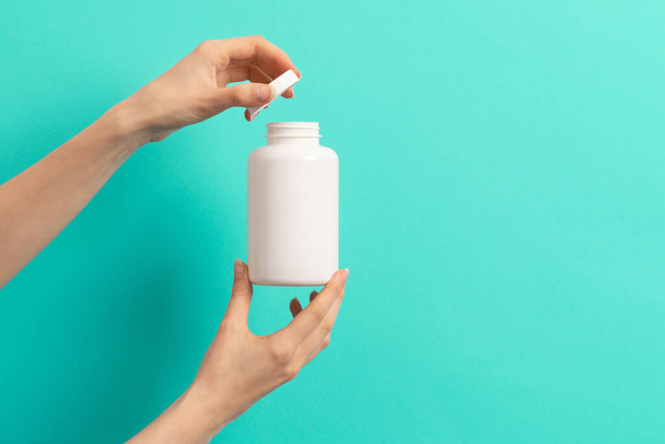 Female hand holding white bottle of medication pills  or vitamins or supplements on green and turquoise background - Foto, imagen