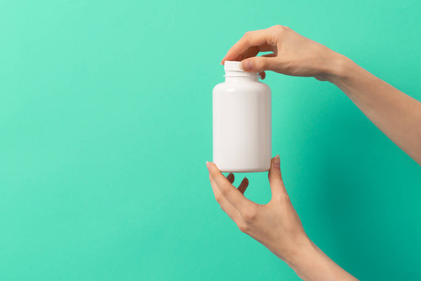 Vrouwelijke hand houden witte fles van medicatie pillen of vitaminen of supplementen op groene en turquoise achtergrond - Foto, afbeelding