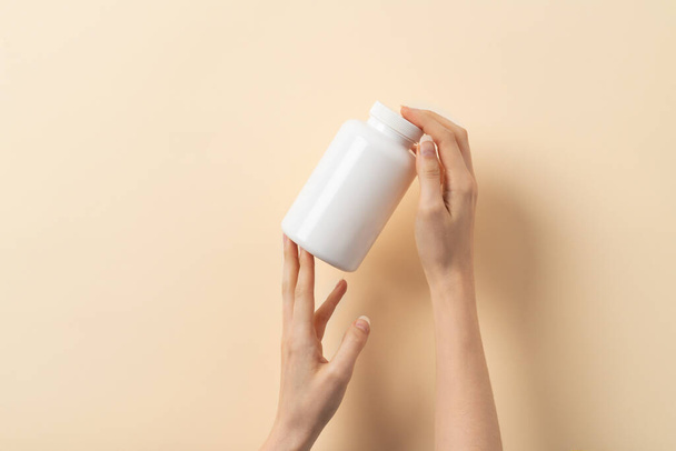 La mano femenina sostiene una botella de píldoras o vitaminas medicamentosas sobre fondo beige - Foto, imagen