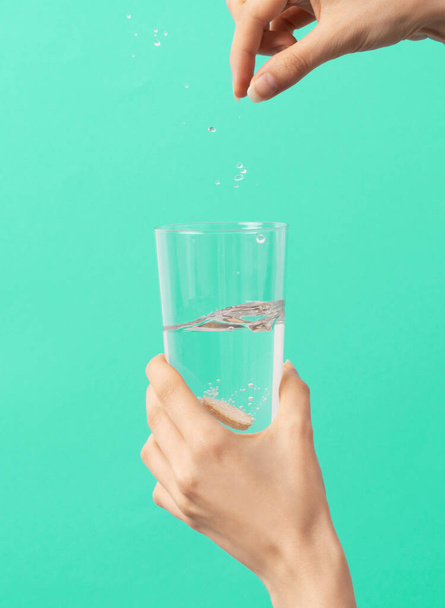 egy női kéz egy pezsgőtablettát dob a kék hátterű pohár vízbe - Fotó, kép