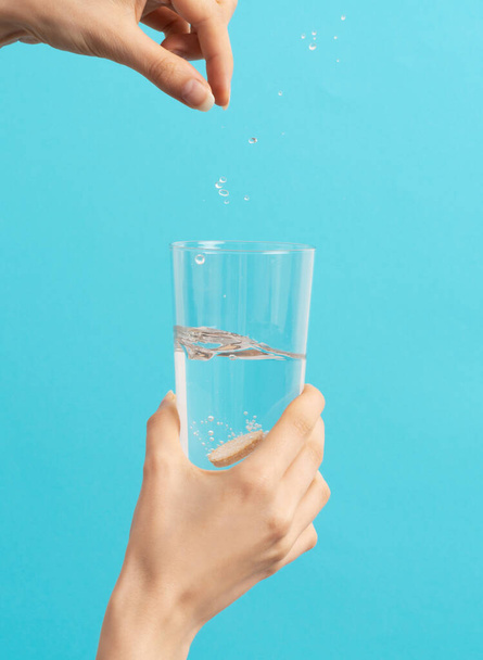 Bir kadın eli mavi arka plandaki su bardağına coşkulu bir tablet düşürür. - Fotoğraf, Görsel
