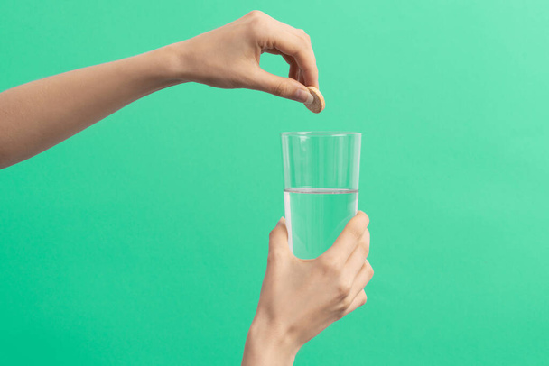 eine weibliche Hand lässt eine Brausetablette in das Wasserglas auf blauem Hintergrund fallen - Foto, Bild
