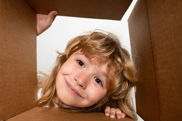 Surprised child boy unpacking, opening carton box and looking inside. The package, delivery, surprise, gift for kid. Children emotions and kids facial expressions concepts. Closeup kids face - Photo, image