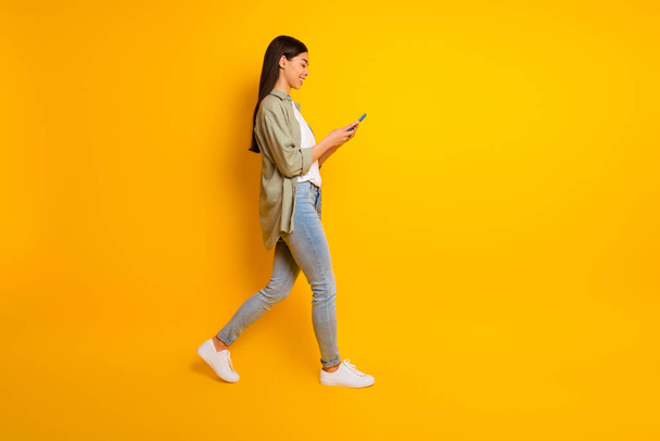 Full body profile portrait of cheerful gorgeous lady walk hold use telephone empty space isolated on yellow color background. - Foto, Imagen