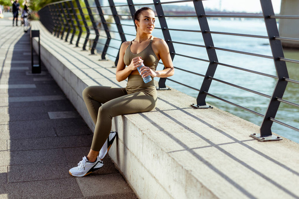 Pretty young woman with earphones takes a break after running in the urban area - 写真・画像