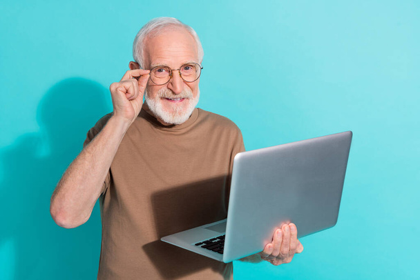 Portrait of attractive cheerful grey-haired man using laptop study learn touching specs isolated over bright blue color background. - Foto, afbeelding